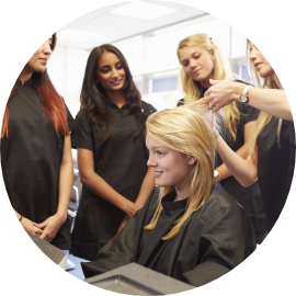 Several women in a salon receiving hair extension training from a professional stylist.